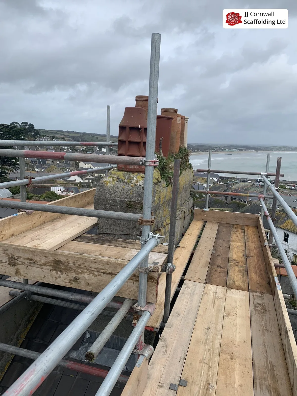 Chimney scaffolding in Cornwall: boarded deck beside a brick chimney stack above the bay