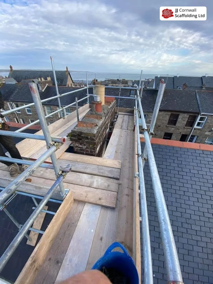 Chimney scaffolding in Cornwall: boarded deck to a chimney over slate with the sea beyond