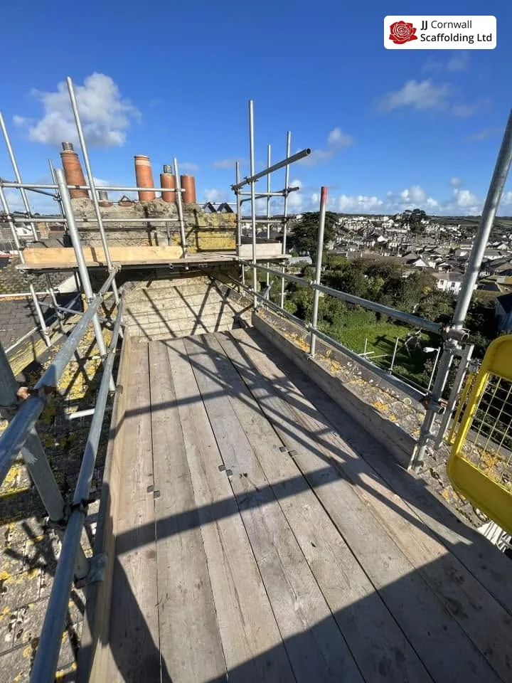 Chimney scaffolding in Cornwall: boarded roof level deck with chimney stacks and town beyond