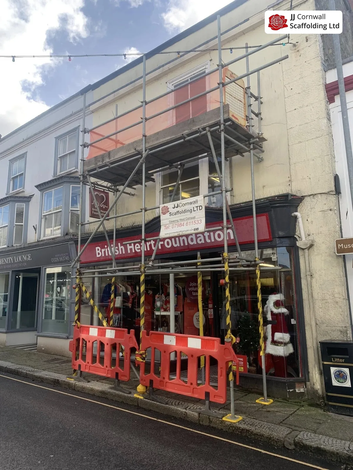 Commercial scaffolding in Cornwall: charity shop frontage red netted lift with pedestrian barriers