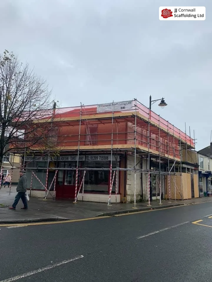 Commercial scaffolding in Cornwall: corner shop red netted top lift on a wet street