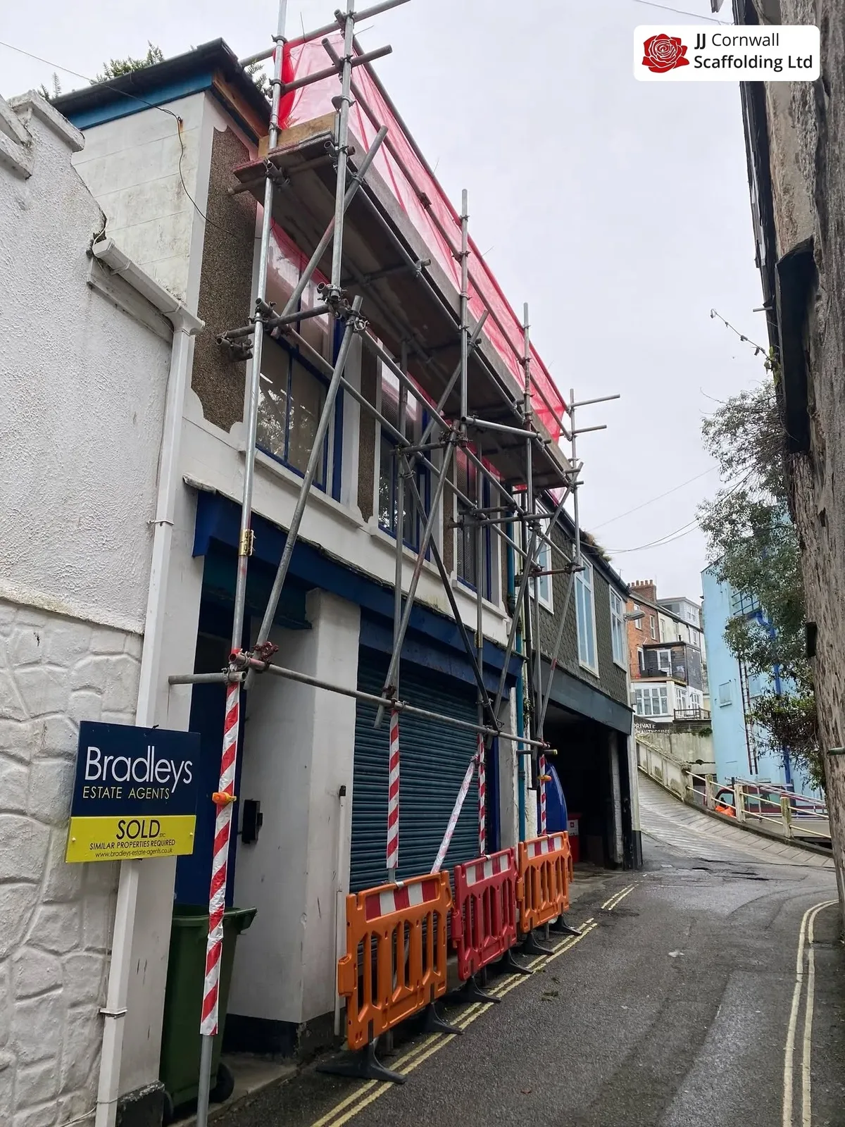 Commercial scaffolding in Cornwall: estate agent frontage red netted lift in a narrow alley