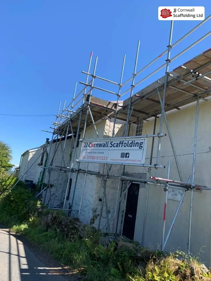 Commercial scaffolding in Cornwall: long granite building roof level run with JJ banner on the lane