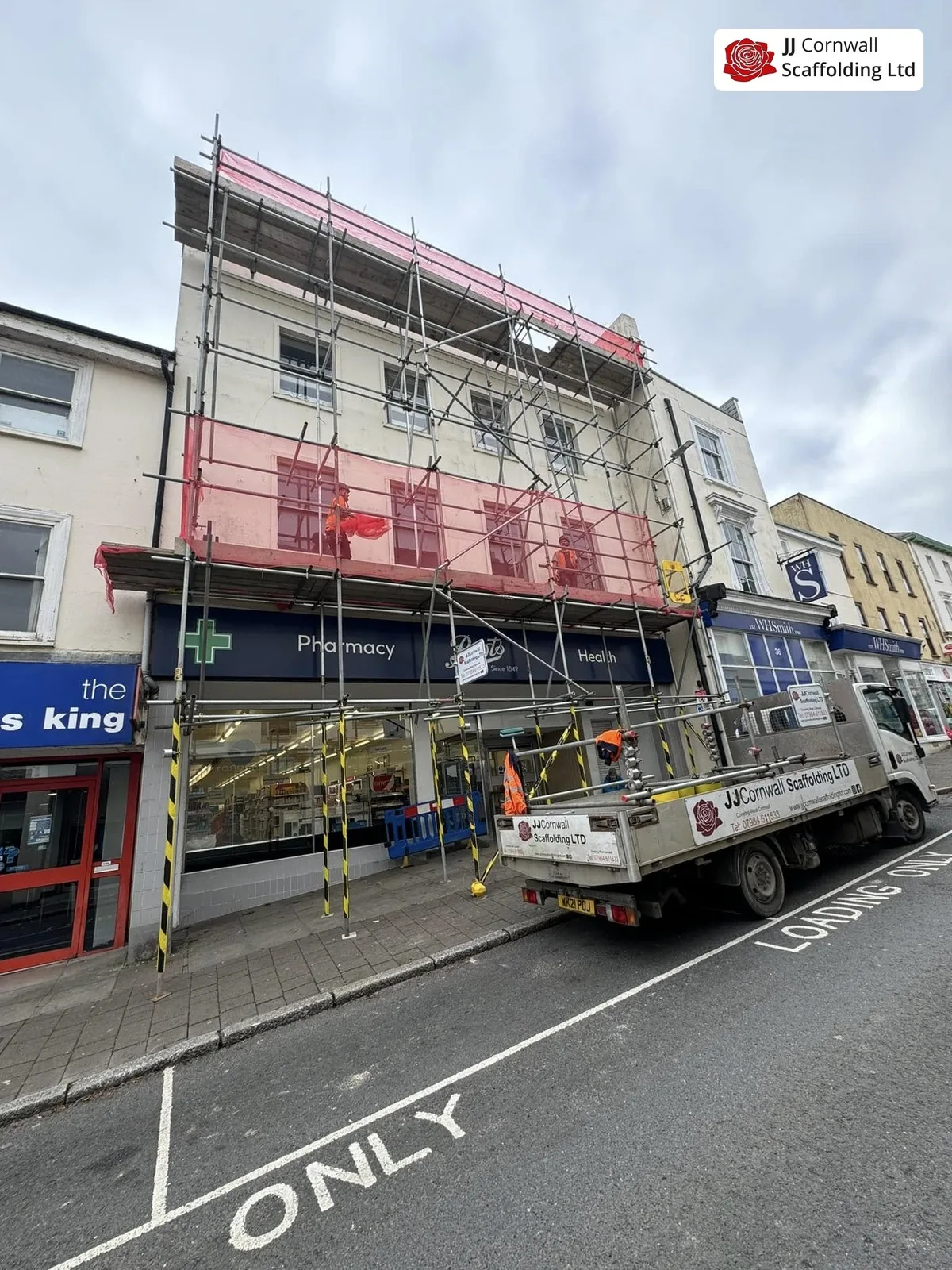 Commercial scaffolding in Cornwall: pharmacy and shop parade red netted lift with JJ lorry loading