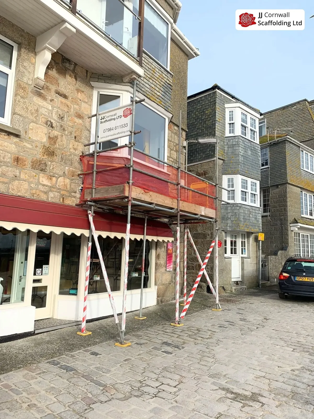 Commercial scaffolding in Cornwall: shop with red awning red netted lift on a cobbled street