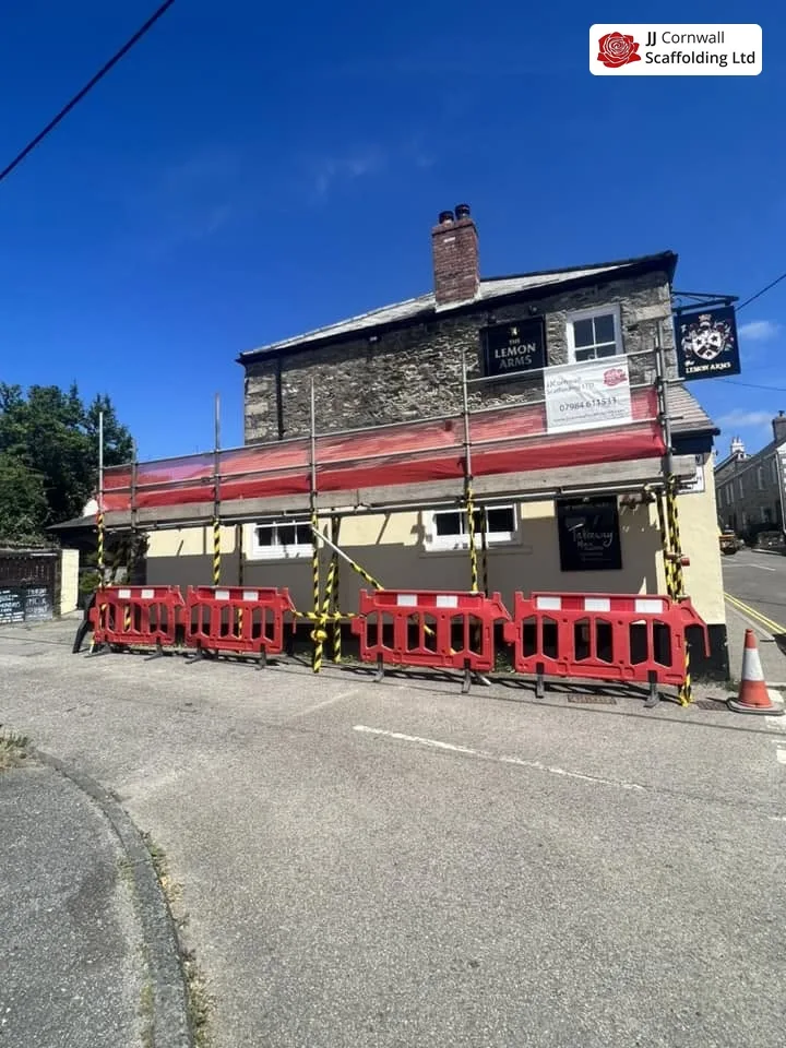 Commercial scaffolding in Cornwall: village pub inn red netted lift with barriers under blue sky