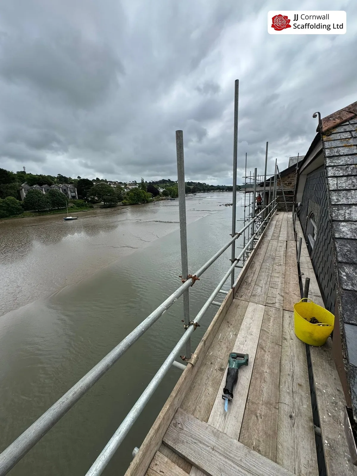 Domestic scaffolding in Cornwall: boarded walkway along estuary wall with lifebuoy