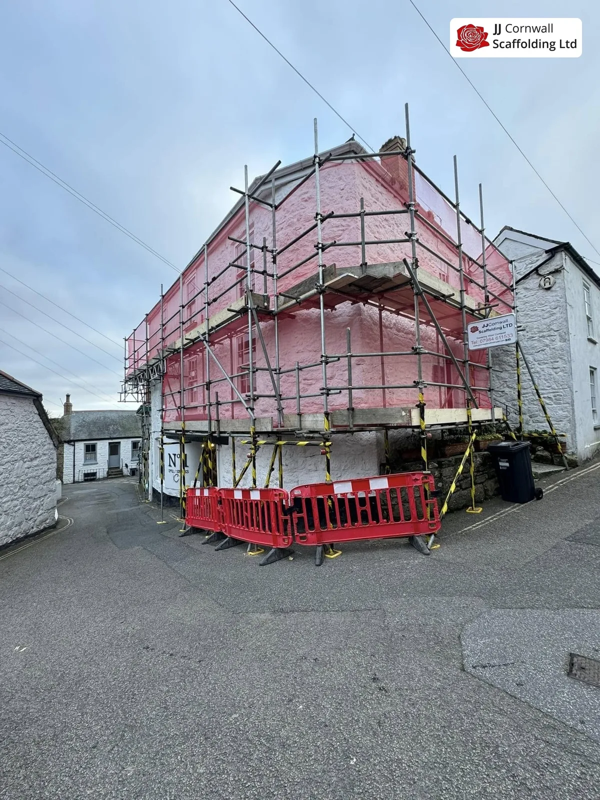 Domestic scaffolding in Cornwall: corner building fully red netted with barriers on a village street