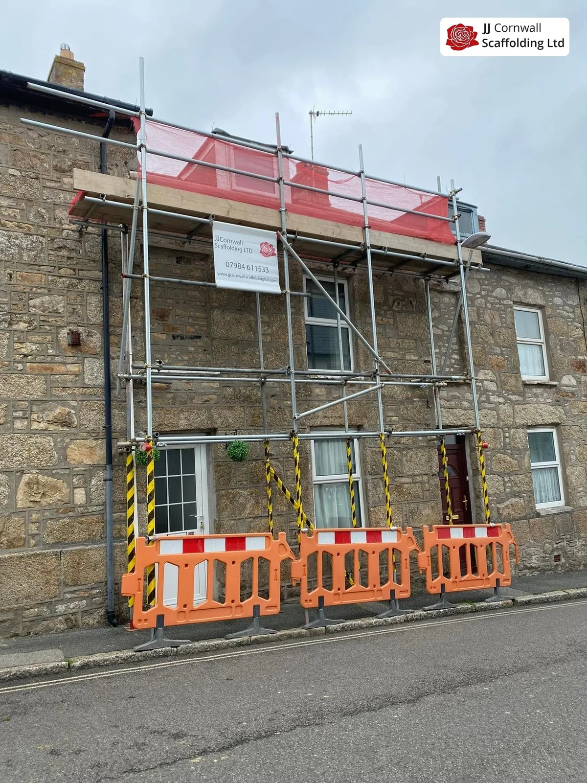 Domestic scaffolding in Cornwall: granite cottage frontage red netting with pedestrian barriers