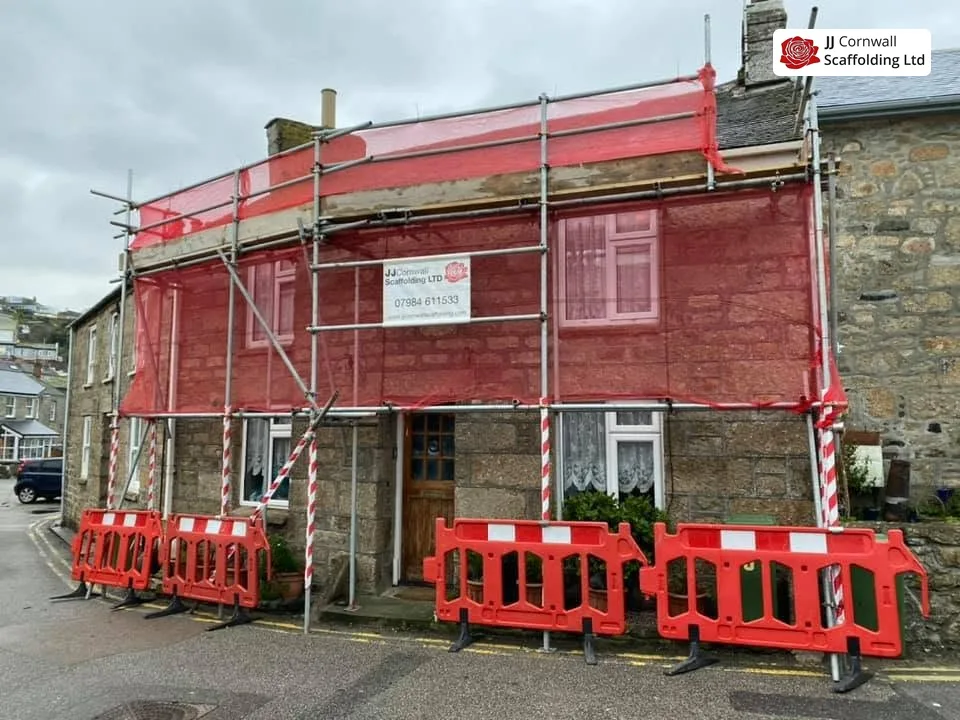 Domestic scaffolding in Cornwall: granite cottage red netted lift with barriers and JJ sign