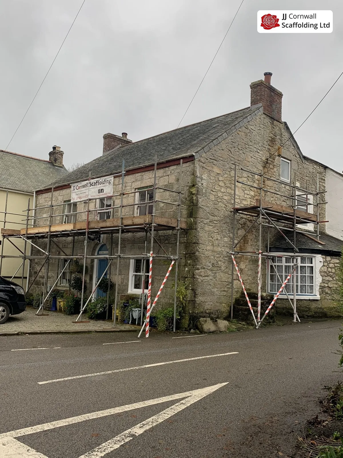 Domestic scaffolding in Cornwall: granite cottage roof level run with JJ banner from the road