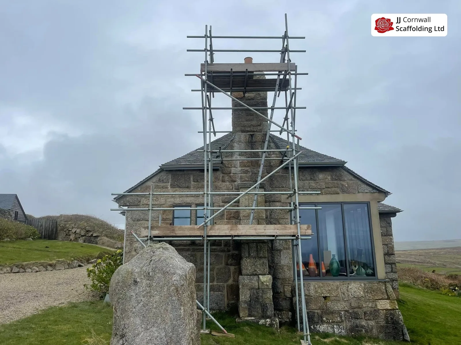 Heritage scaffolding in Cornwall: granite coastal lookout chimney scaffold beside standing stone