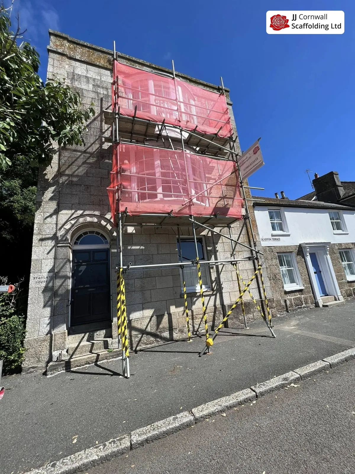 Heritage scaffolding in Cornwall: granite hall arched door red netted lift on a corner