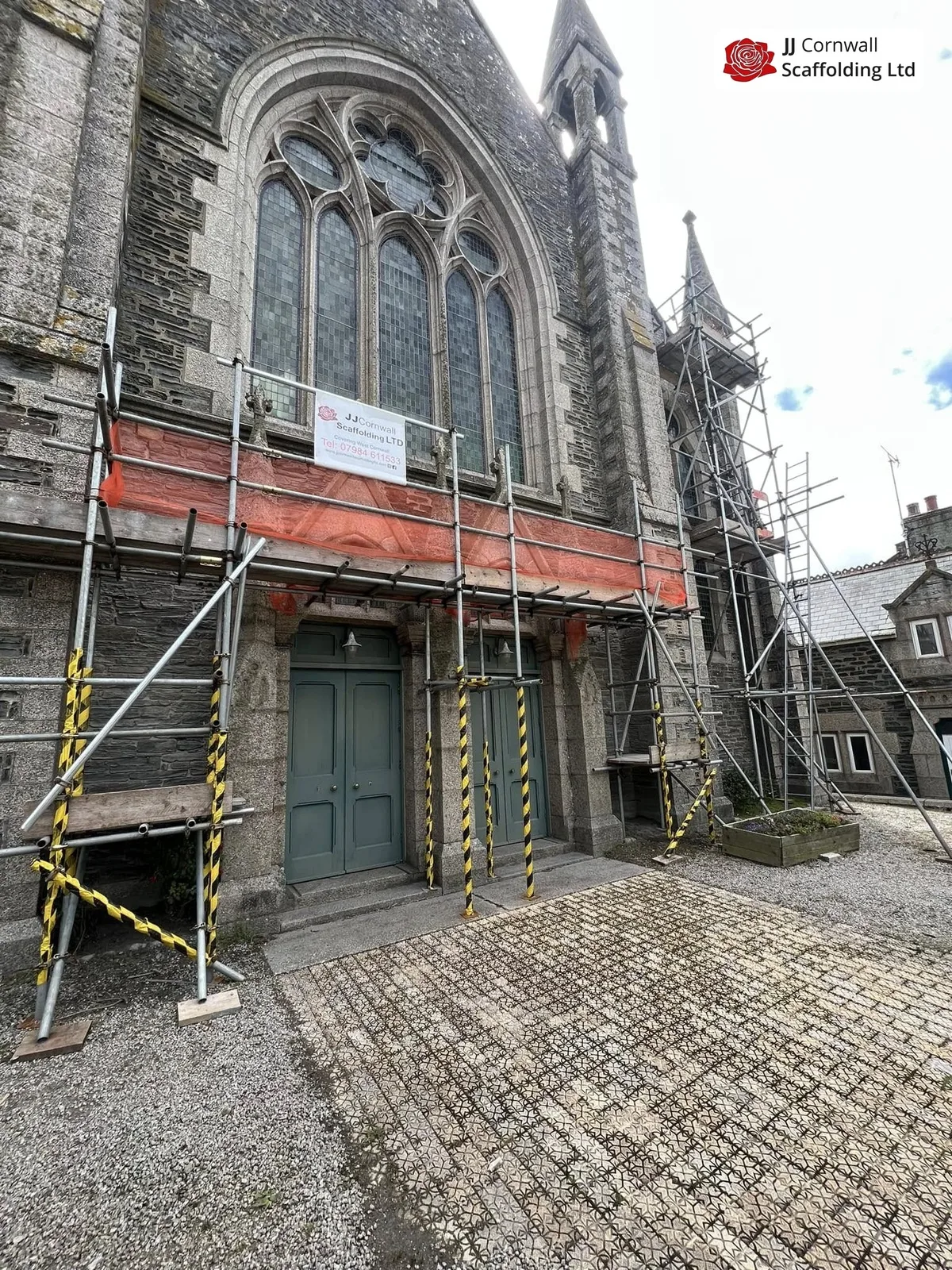 Heritage scaffolding in Cornwall: listed church gothic arched window red sheeted lift with JJ banner
