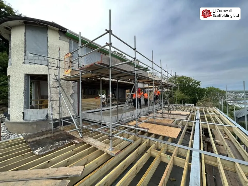Scaffold hire in Cornwall: roof level deck over exposed joists with operatives and coastal view